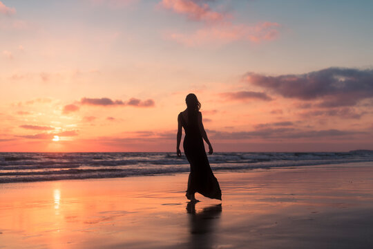 Relaxed woman walking on the beach shore at sunset