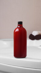 Red bottle of bubble bath and towels on tub indoors