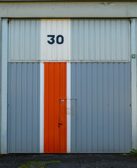 closed door of a pavilion, of an industrial warehouse in a polygon, gray door, an orange vertical stripe and the number thirty painted metal painted with vertical stripes,