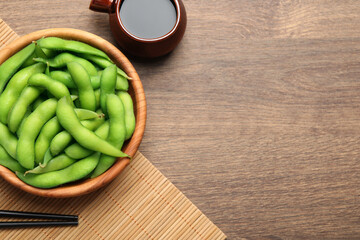 Green edamame beans in pods served with soy sauce on wooden table, flat lay. Space for text