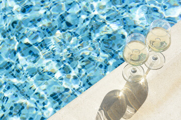 Glasses of tasty wine on swimming pool edge, space for text