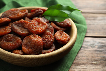 Bowl of tasty apricots and green leaves on wooden table, closeup. Dried fruits