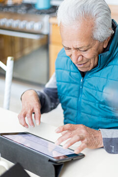Modern older adult surfing the internet at house with a tablet