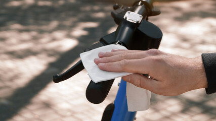 Man cleaning scooter steering wheel with wet wipe outdoors, closeup. Protective measures © New Africa