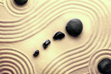 Fototapeta na wymiar Black stones on sand with pattern, top view. Zen, meditation, harmony