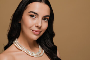 Young woman wearing elegant pearl necklace on brown background, space for text