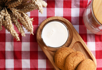 Glass of milk with cookies on red checkered tablecloth, flat lay