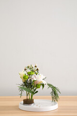 Fototapeta na wymiar Beautiful ikebana on wooden table near light wall