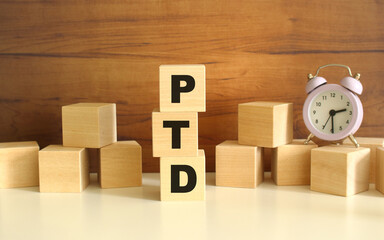 Three wooden cubes stacked vertically on a brown background make up the word PTD.