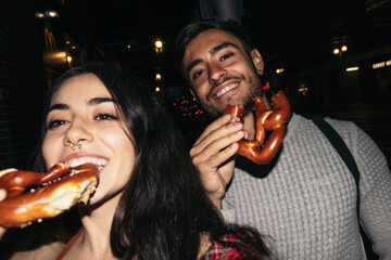 Happy couple eating pretzel at night