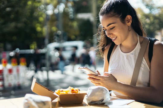 Woman chatting with smartphone while eating outdoors