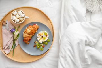 Wooden tray with delicious breakfast and cup of hot cacao on bed