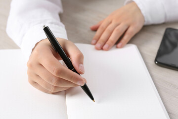 Woman writing in notebook at wooden table, closeup