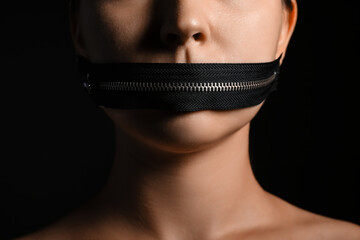 Young woman with zipper on her mouth against dark background, closeup. Censorship concept - obrazy, fototapety, plakaty