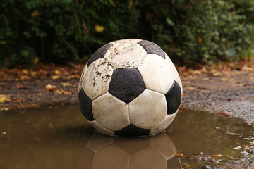 Fototapeta na wymiar Dirty soccer ball in muddy puddle outdoors