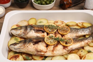 Baking tray with delicious baked sea bass fish and potatoes on table, closeup