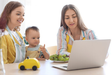 Happy lesbian couple with their little baby and laptop at table in kitchen