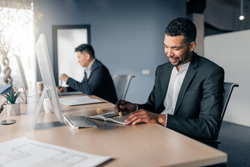 African businessman taking notes during working day in office on colleague background