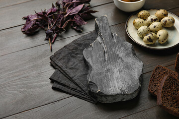 Cutting board with napkin, quail eggs, bread and basil on dark wooden background