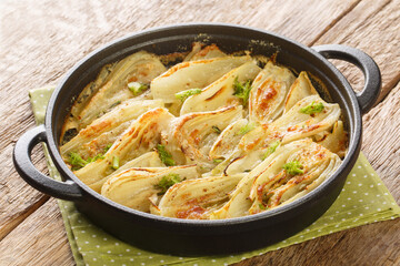 Baked fennel root with parmesan cheese and bechamel sauce close-up in a frying pan on the table. Horizontal