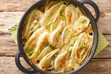 Baked fennel root with parmesan cheese and bechamel sauce close-up in a frying pan on the table. Horizontal top view from above