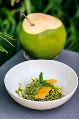 Spaghetti with pesto and coconut under palm leaf
