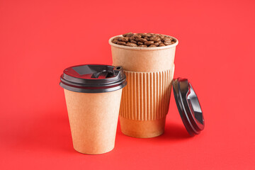Paper cups with coffee beans on red background
