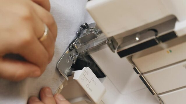 A woman designer works on an overlock sewing machine on tailoring. Close-up. Vertical frame. Small tailoring business.