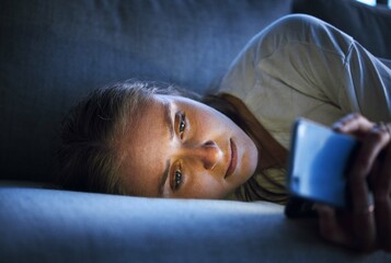Phone, night and sad woman relaxing on sofa in living room scrolling on social media after a break up. Depression, upset and girl on couch in lounge reading student loan or debt emails on smartphone.