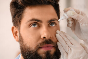 Ophthalmologist putting drops in young man's eye at hospital, closeup