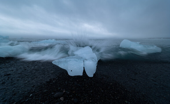 Block of ice being hit by a wave at J&ouml;kuls&aacute;rl&oacute;n beach, Iceland.