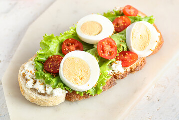 Board of tasty toast with boiled egg and tomatoes on light background, closeup