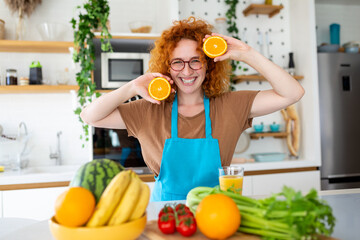 Photo of cute caucasian woman smiling and holding two orange parts while cooking vegetable salad in kitchen interior at home