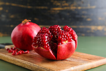 Cutting board with fresh pomegranates on color wooden table, closeup