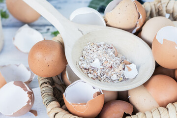 Brown and white crushed eggshells in wooden spoon on whole eggshells in basket on white table, natural calcium source, sustainability concept