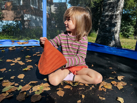 Small girl holding her beanie hat is sitting on a trampoline 