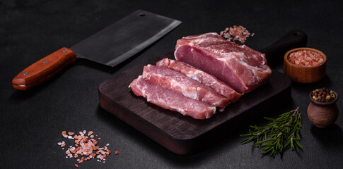 Fototapeta na wymiar Fresh piece of raw pork with spices, salt and herbs on a wooden cutting board