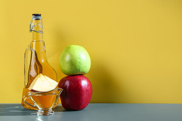 Bottle and gravy boat of apple cider vinegar on table near color wall