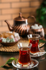 Saucer with glass of Turkish tea and leaf on table in room, closeup