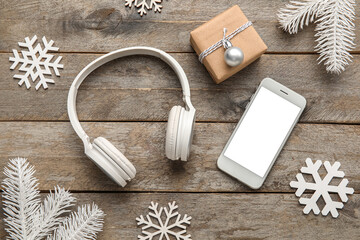 Modern headphones, mobile phone, Christmas gift and decorations on wooden background