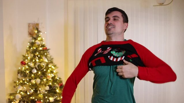 Excited male putting on Christmas jumper looking at camera sad finding it's the wrong size fitting, short sweater slow motion