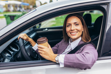 Young businesswoman driving in a car to work during the day, drink coffee.