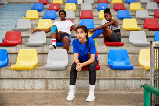 Fit diverse sportswomen resting on stadium tribune