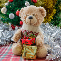 Small teddy bear with gift boxes in front of Christmas tree