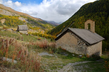 Fototapeta na wymiar The hamlet Le Villard located along the Cristillan valley above Ceillac, Queyras Regional Natural Park, Southern Alps, France, with Sainte Barbe chapel, a traditional wooden chalet and Autumn colors