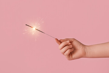 Female hand with festive Christmas sparkler on pink background, closeup