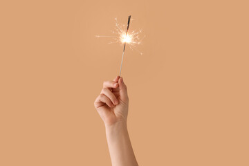 Female hand with burning Christmas sparkler on color background