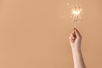 Female hand with burning Christmas sparklers on color background