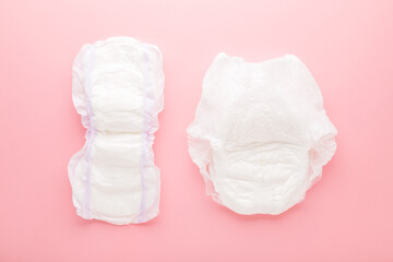 White big size sanitary towel and diaper pant on light pink table background. Pastel color. Closeup. Hygiene product for urinary incontinence or after childbirth. Top down view. - obrazy, fototapety, plakaty
