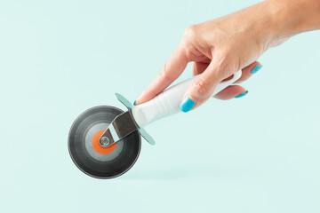 Woman’s hand holding pizza cutter with vinyl record on isolated pastel background. Minimal...